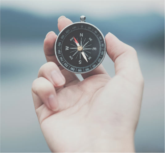 A hand holds a compass in front of a canadian landscape to respresent navigating the canadian immigration application procedure.